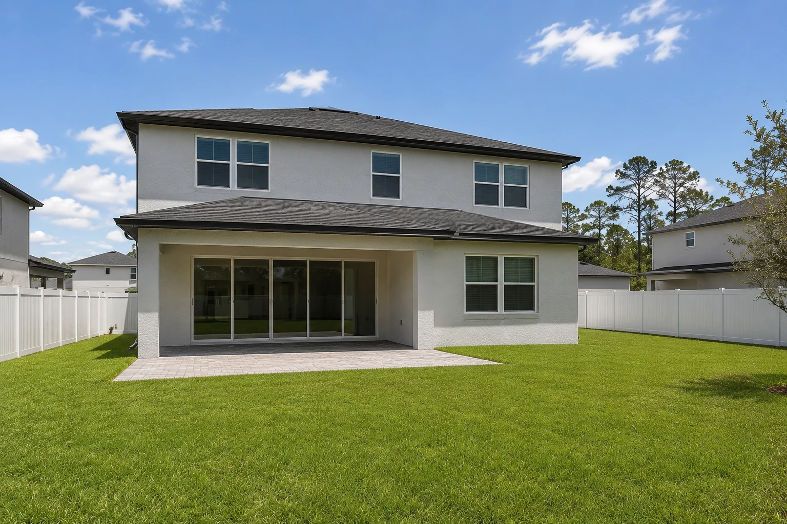 Two-story home with an empty backyard and plain paver patio before renovation